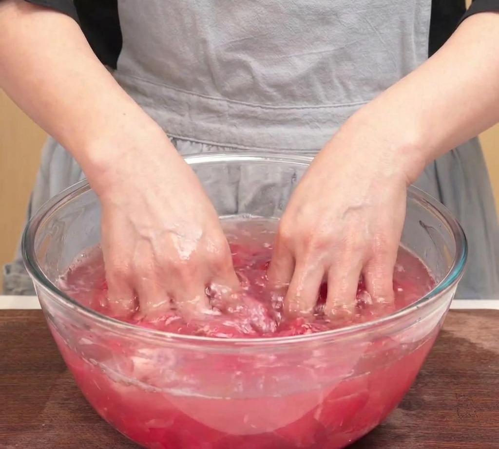 Hands squeezing a batch of rinsed raw beef slices over a glass bowl to remove excess water.