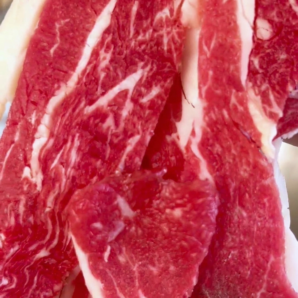 A close-up view of fresh, marbled raw beef slices piled inside a large stainless steel mixing bowl.