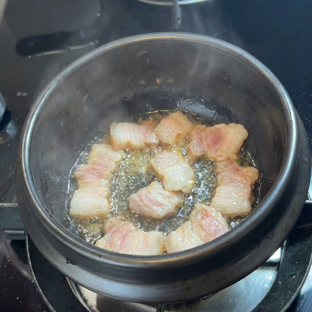 Slices of pork belly sizzling in their own fat at the bottom of a black stone pot.