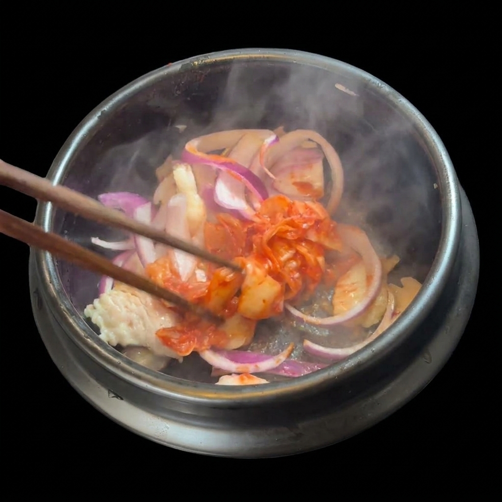 A handful of chopped red kimchi being added to the sautéed pork and onions in the stone pot.