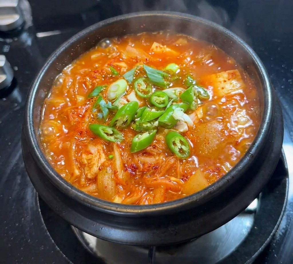 Freshly sliced green chili peppers and some scallions scattered on top of the bubbling surface of a kimchi stew.