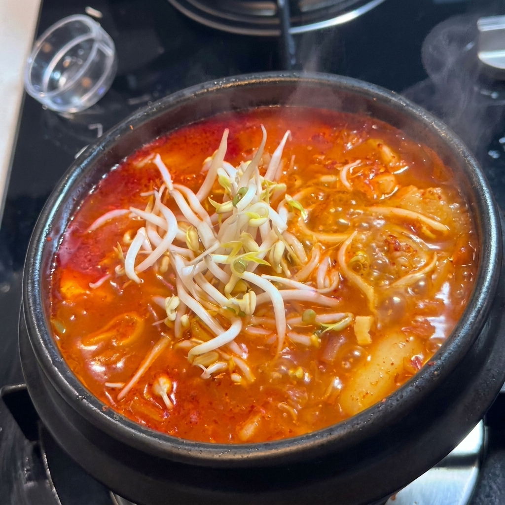 A mound of fresh, white bean sprouts placed on top of a simmering black pot of red kimchi soup.