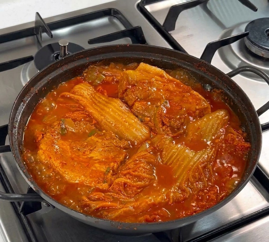 Two thick slabs of raw pork belly resting on a bed of sliced white onions in a black cooking pan on a stove.