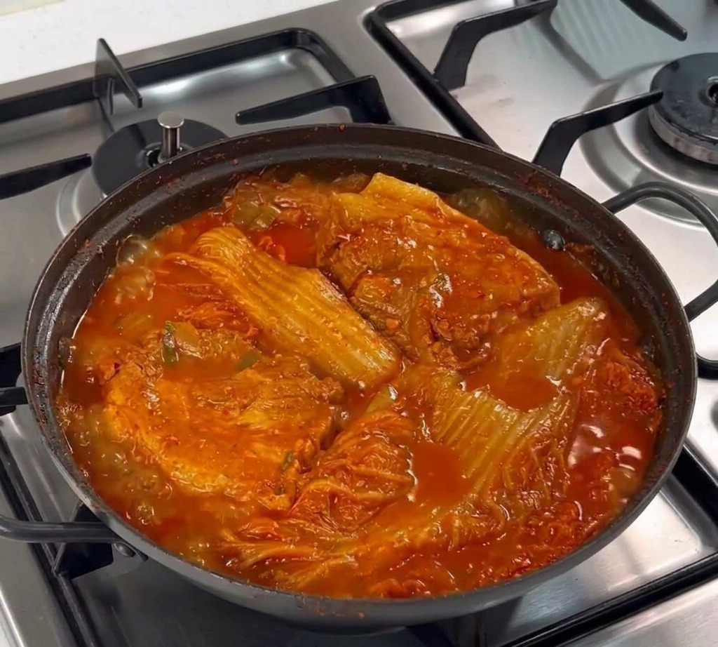 A metal spoon placing a mound of minced garlic onto the surface of raw pork belly in a pan.