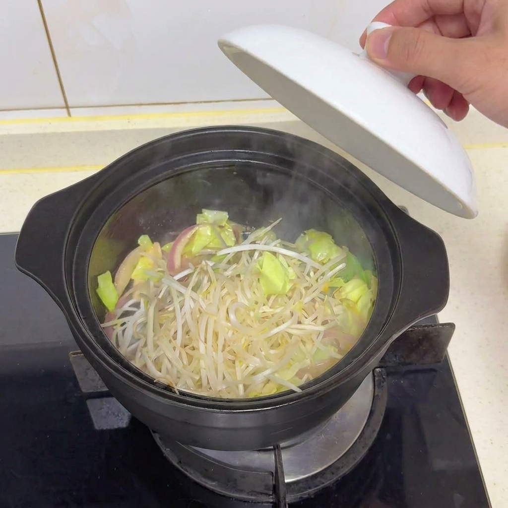 Fresh bean sprouts resting on top of cooked cabbage inside a dark pot with the lid being lifted.