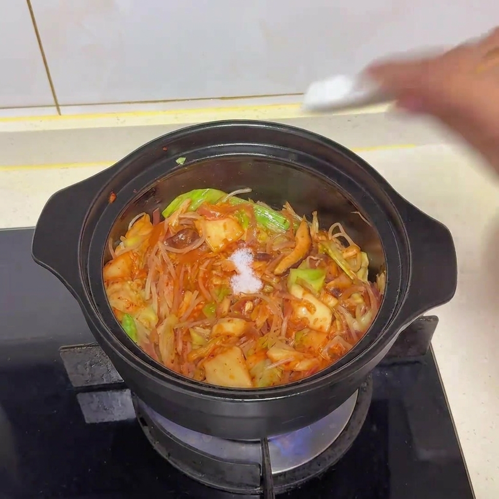 A pinch of white salt being added into the pot of stir-fried vegetables and kimchi.