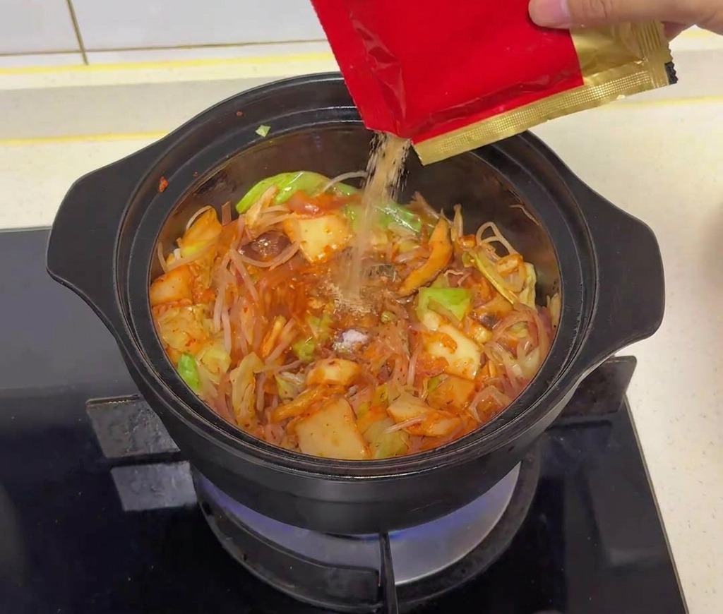 Tan beef seasoning powder being poured from a red and gold packet into the vegetable mixture in the pot.
