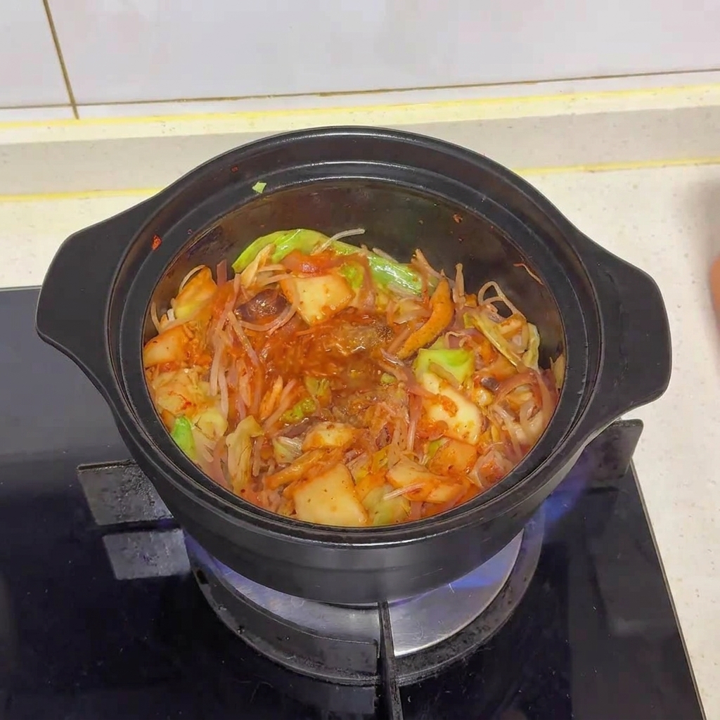 The vegetable and kimchi mixture in the pot after beef powder and MSG have been added, showing the wet seasonings beginning to meld.