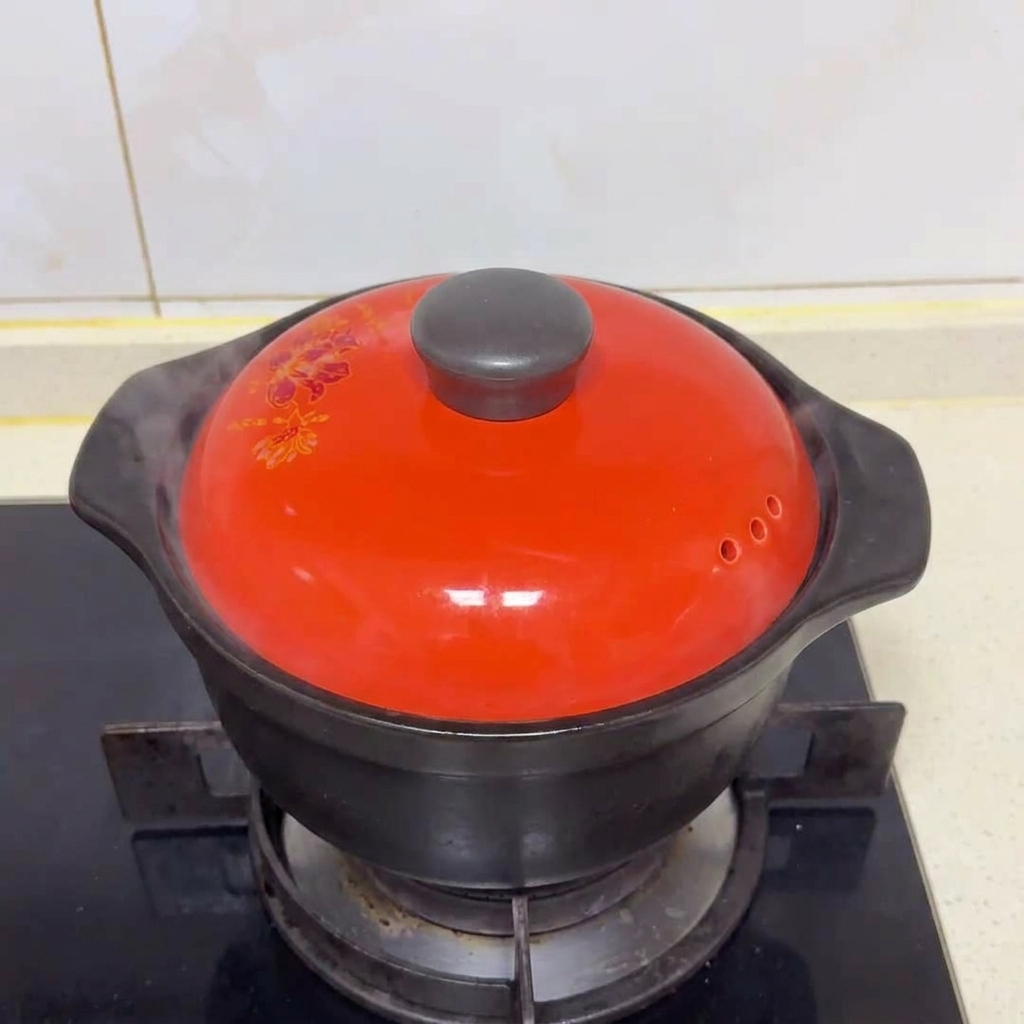 A vibrant red ceramic lid covering a black cooking pot on a gas stove with steam escaping from the side.