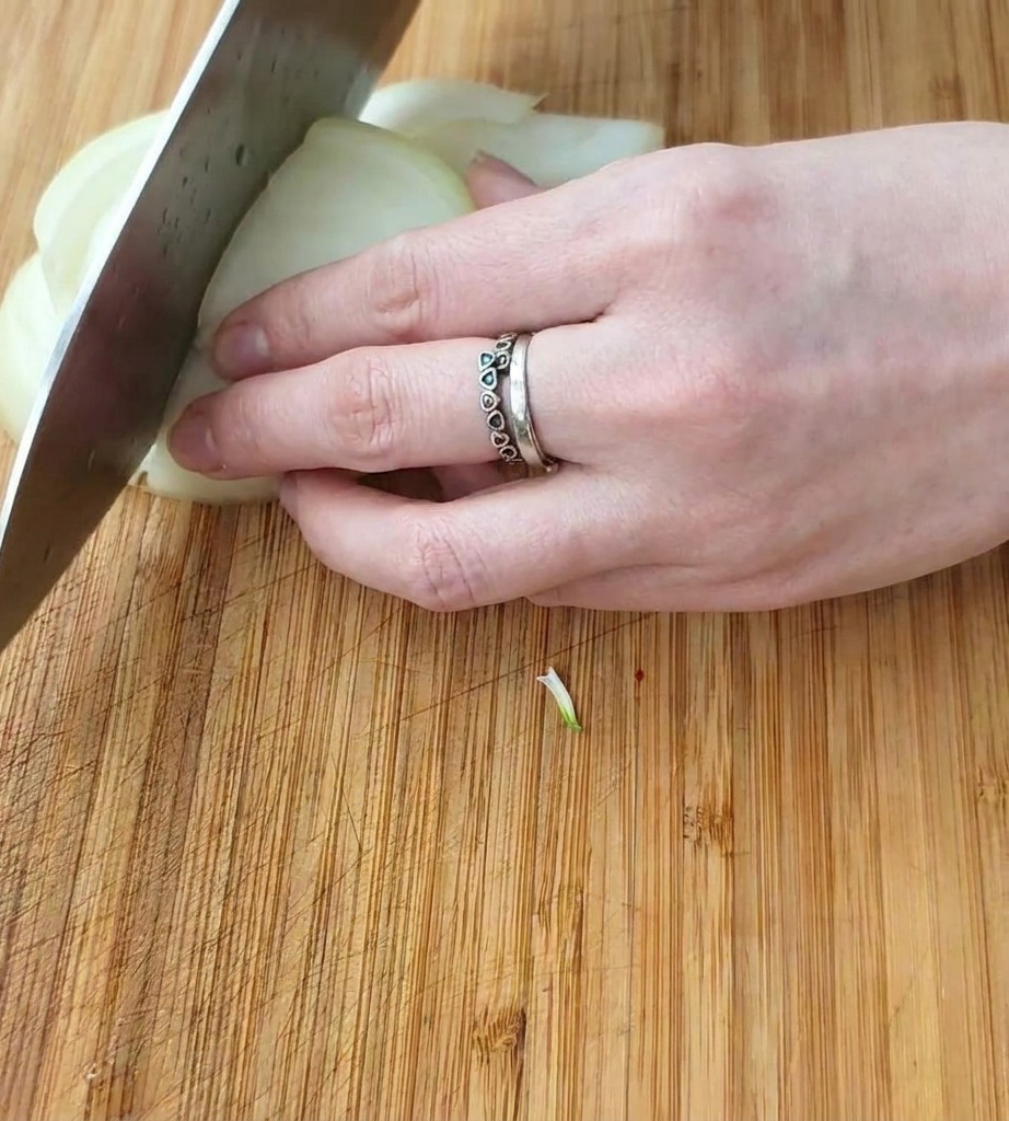 A close-up shot of a hand using a chefs knife to slice a white onion into square chunks on a wooden board.