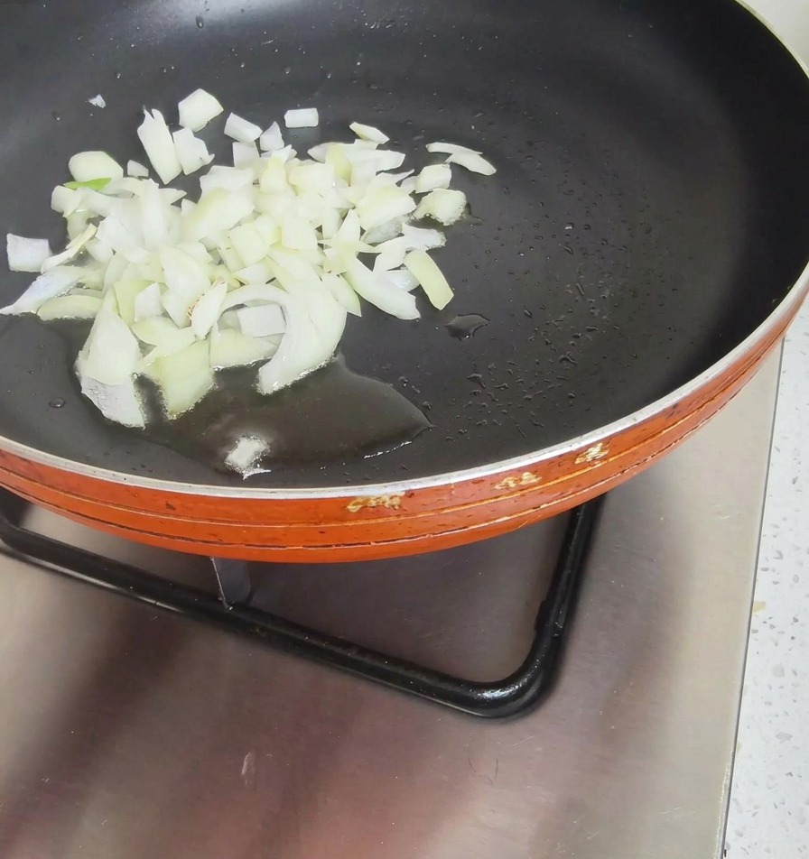 A heap of chopped white onions sitting in a small pool of oil in the center of a dark non-stick frying pan.