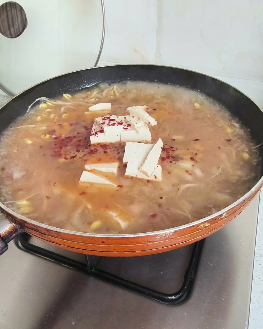Bright red chili flakes scattered across the top of a simmering soup containing tofu and bean sprouts.