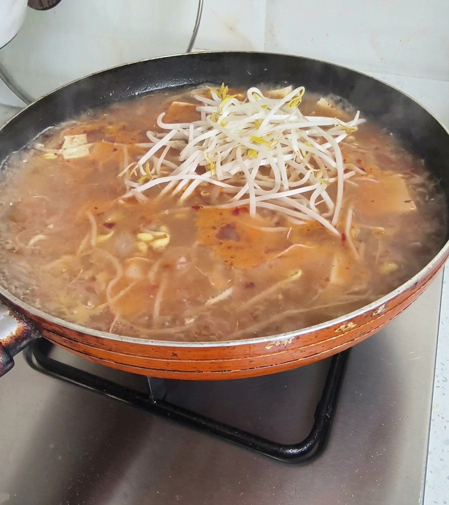 A generous pile of fresh, white bean sprouts being placed on top of a bubbling pan of soup.