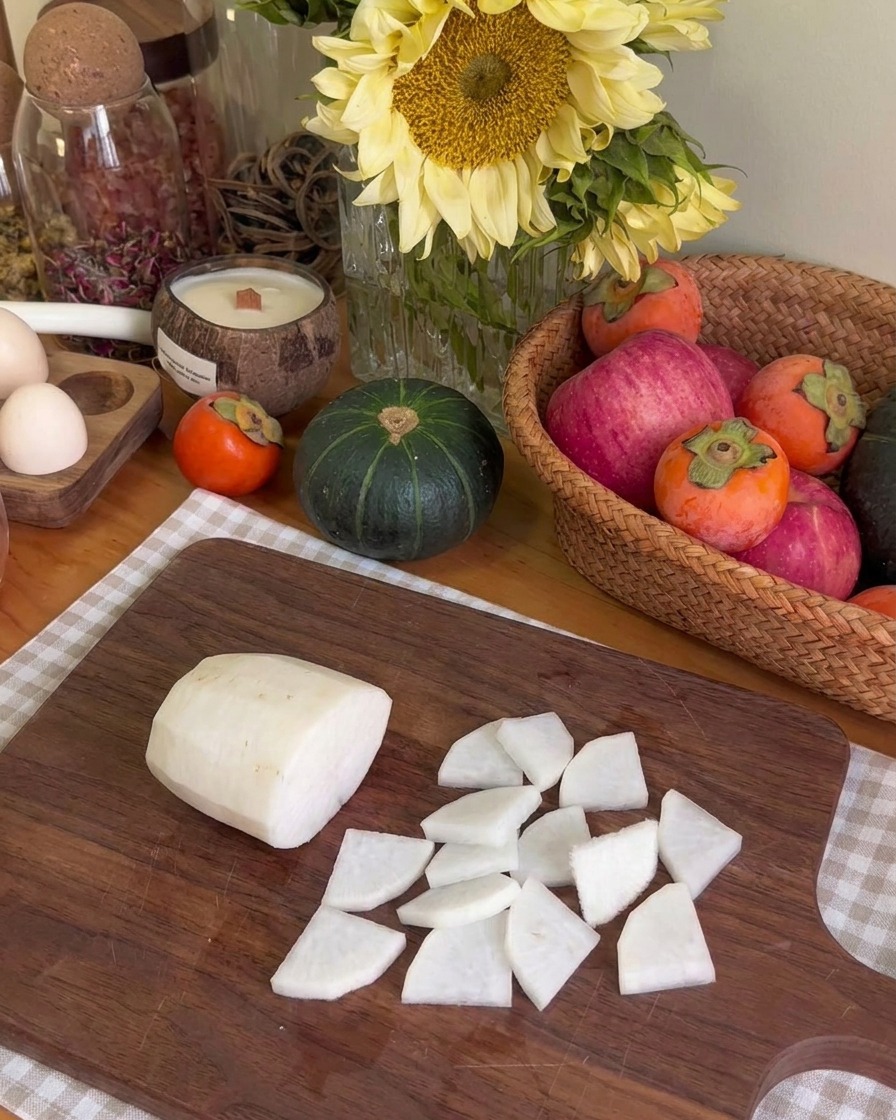 Thinly sliced pieces of white radish arranged on a wooden cutting board next to a larger piece of raw radish.