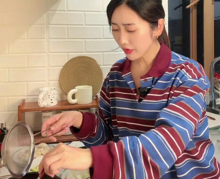 Brown soybean paste being stirred through a fine mesh strainer into a pot of boiling water using a metal spoon.