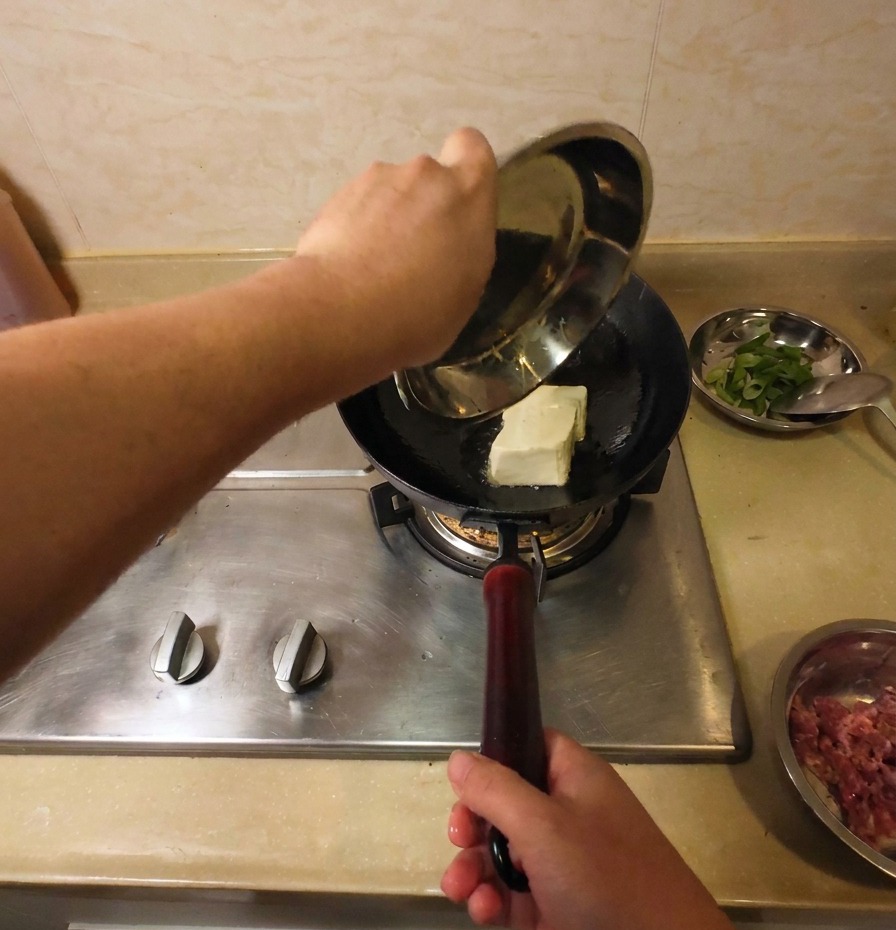 A solid block of white tofu being added into a wok of hot oil to begin the frying process.