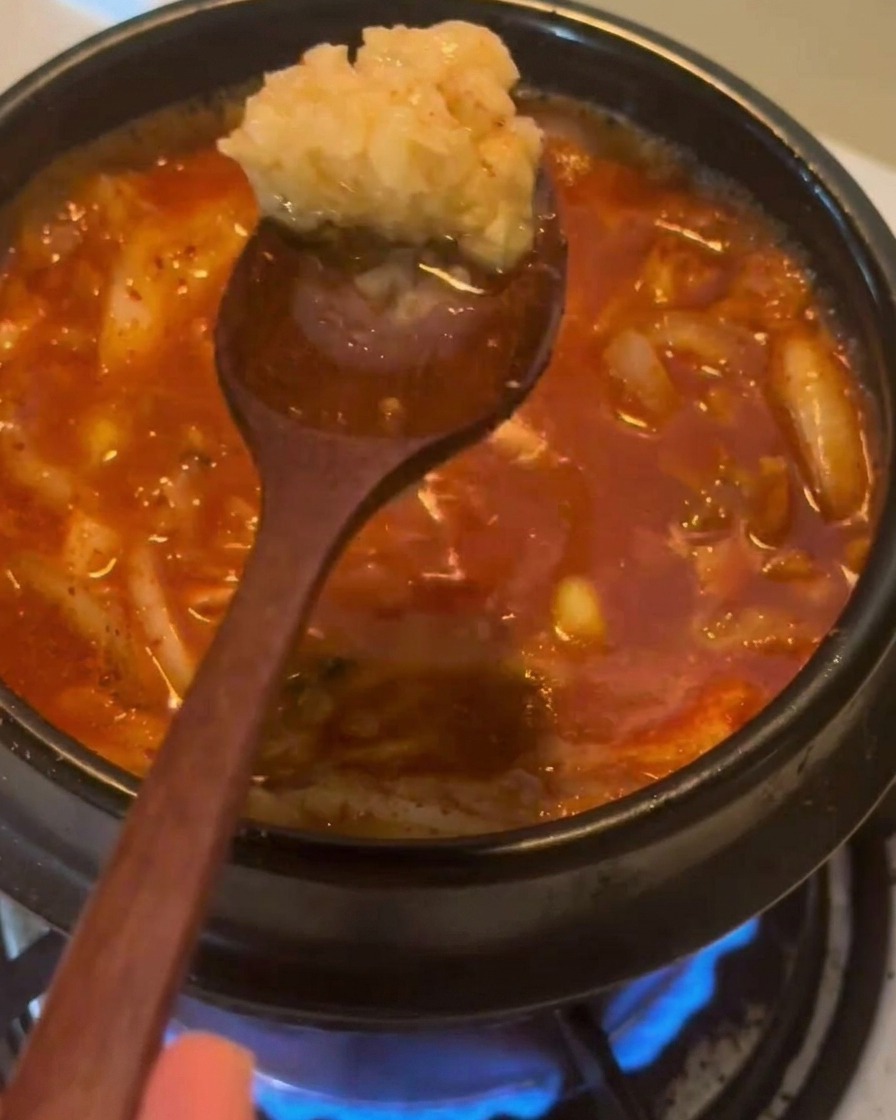 A wooden spoon holding a large dollop of minced garlic over a bubbling red stew.