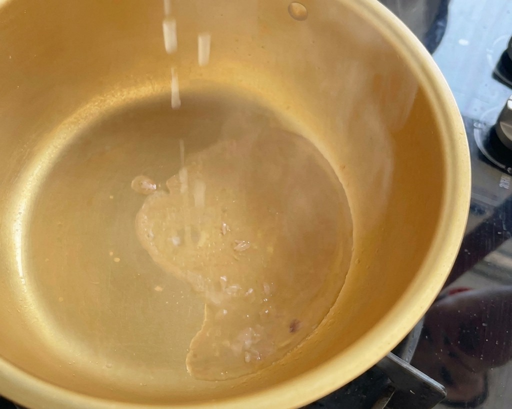 Chopped green onion pieces falling into a steaming gold pot containing hot tuna oil.