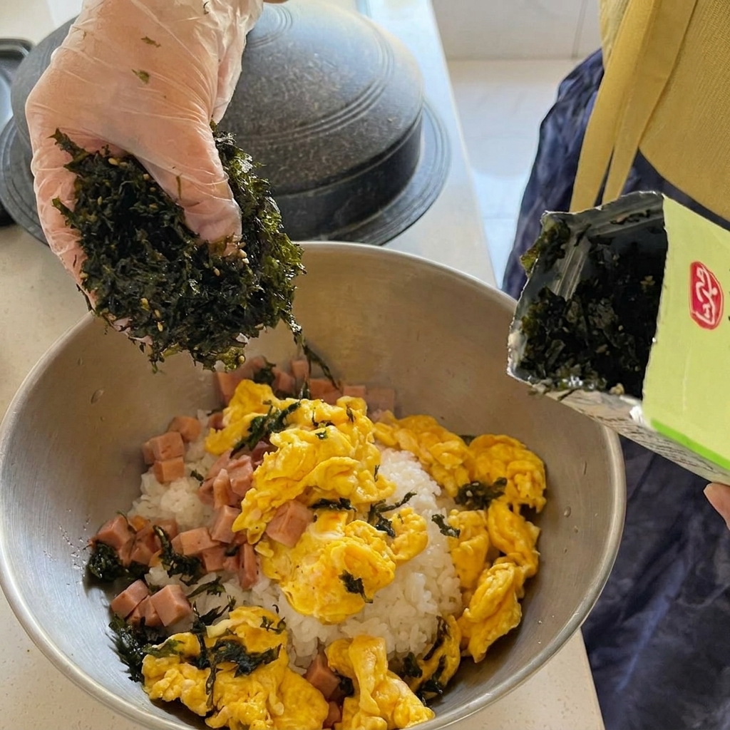 Large chunks of canned tuna being added into a vibrant red, bubbling kimchi stew in a gold pot.