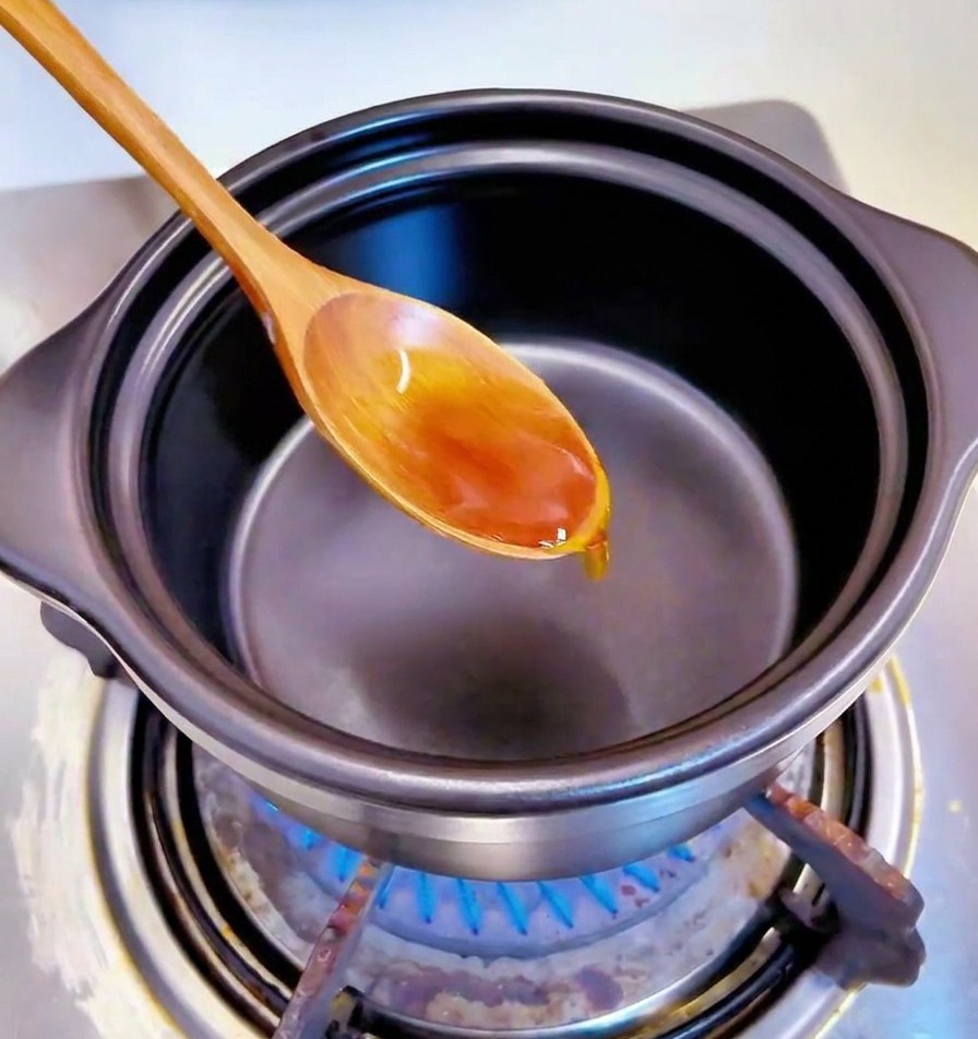 A wooden spoon stirring small pieces of minced garlic in oil at the bottom of a black pot.
