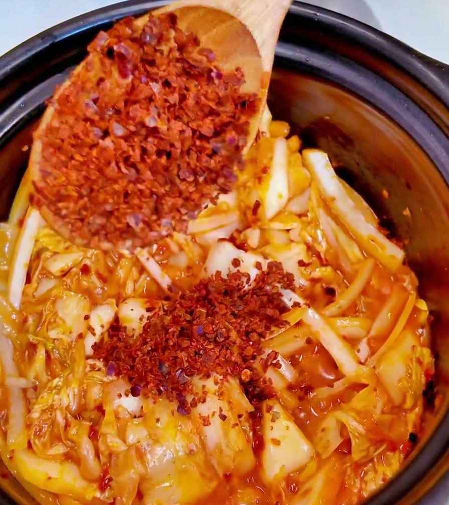 Adding a spoonful of fine red chili powder into the pot with kimchi and aromatics.