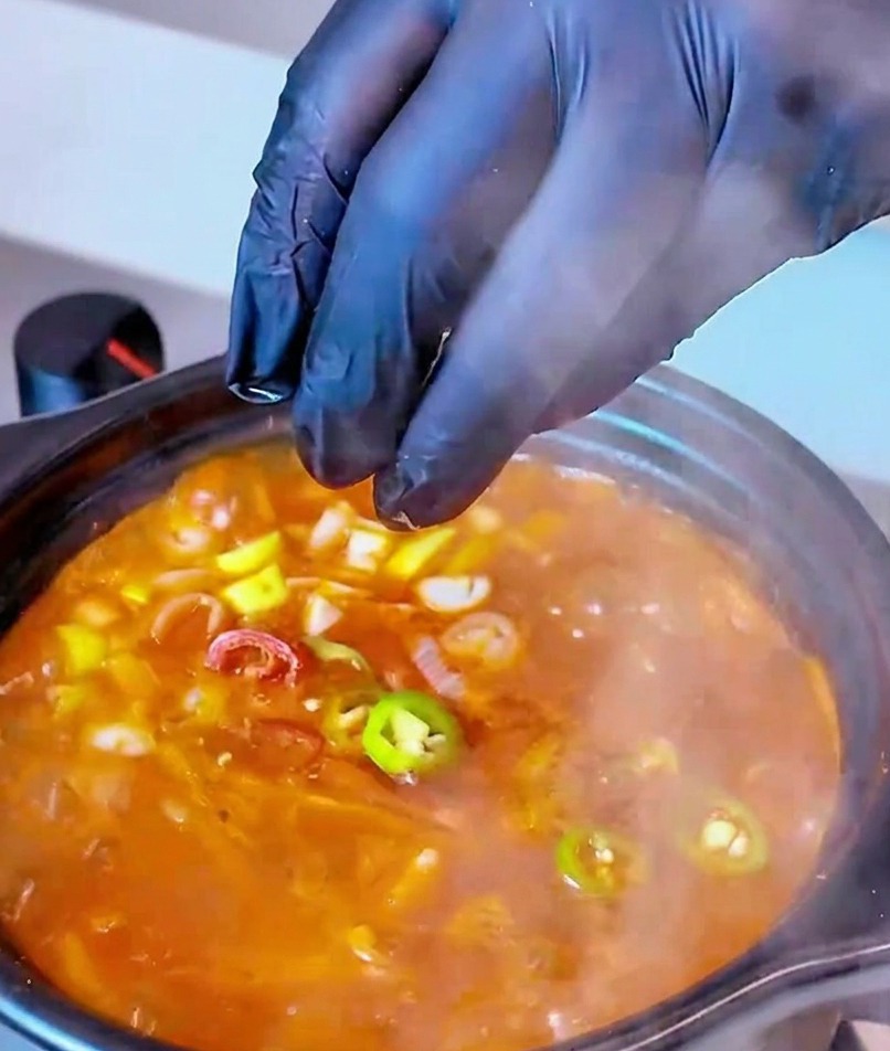 Freshly sliced red and green chili pepper rounds being dropped into a bubbling pot of Tuna Kimchi Soup as a final garnish.