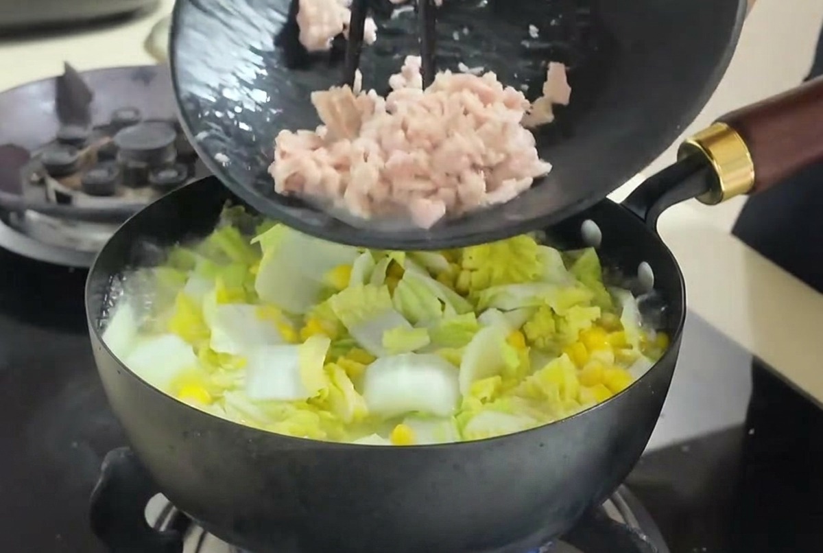 Flaked tuna being scraped from a black plate with chopsticks into a bubbling vegetable soup.