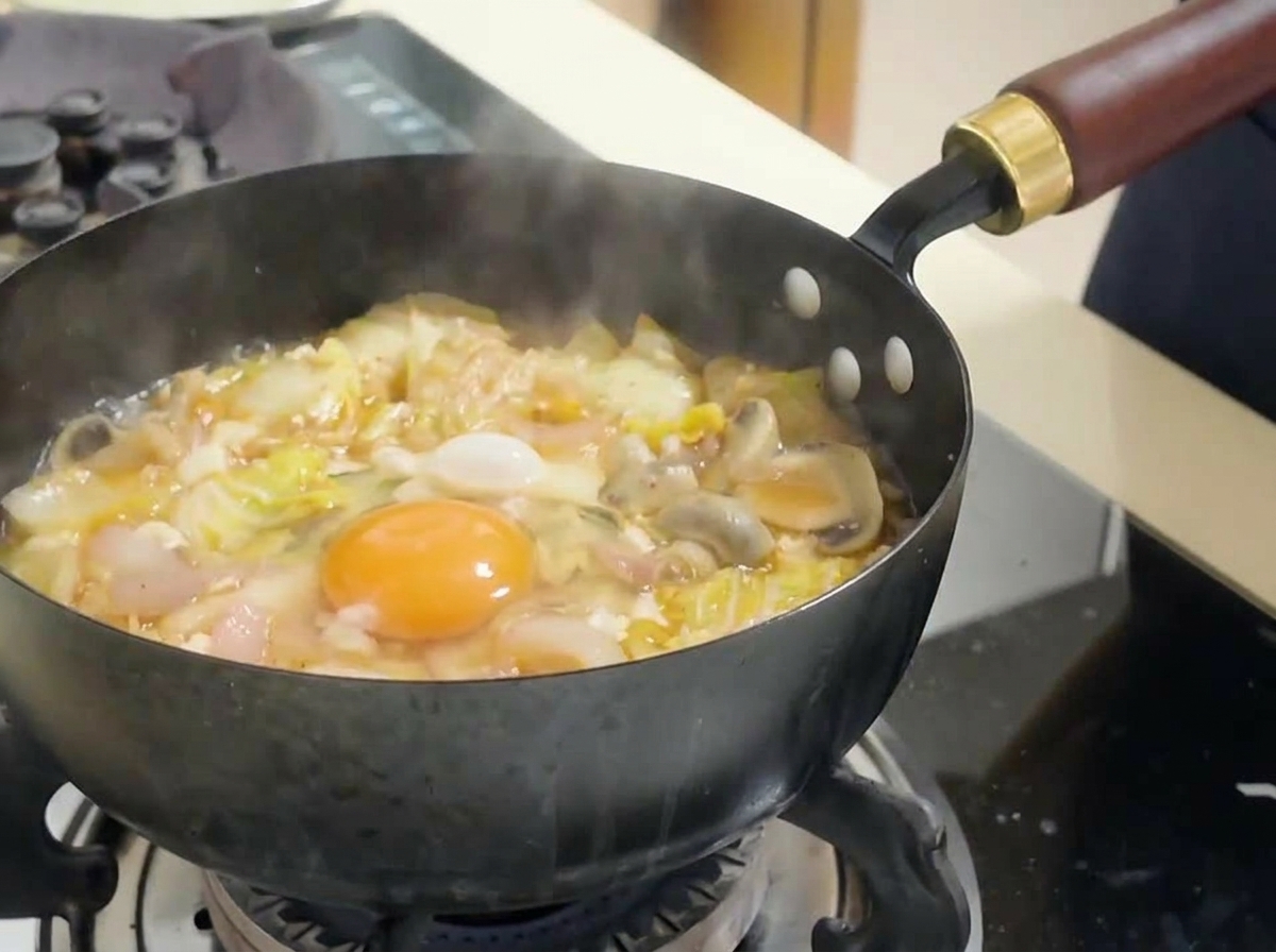 A whole raw egg yolk resting in the center of a pot of boiling red kimchi soup, surrounded by napa cabbage and tofu.