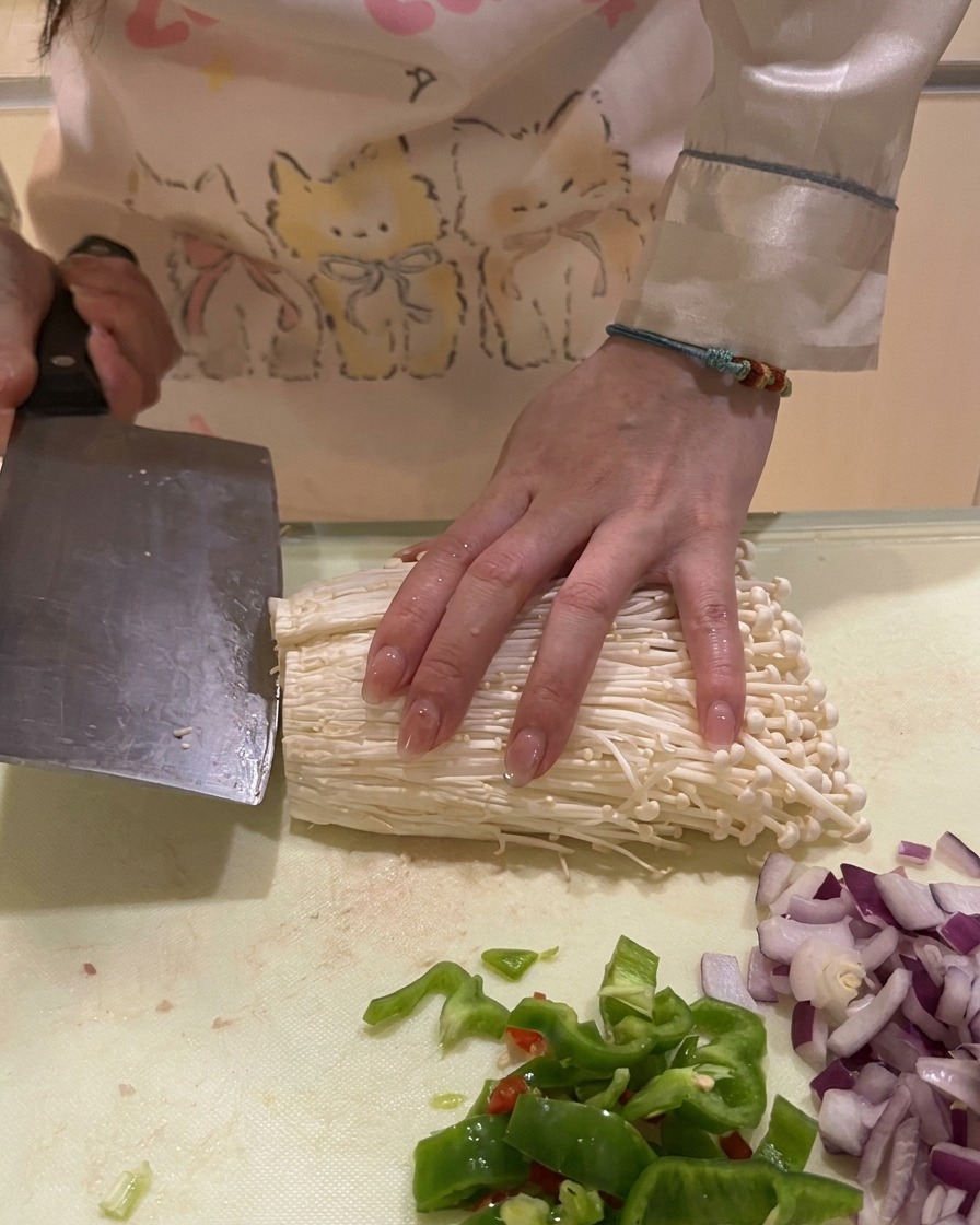 Cutting the bottom roots off a bundle of white enoki mushrooms on a kitchen counter.