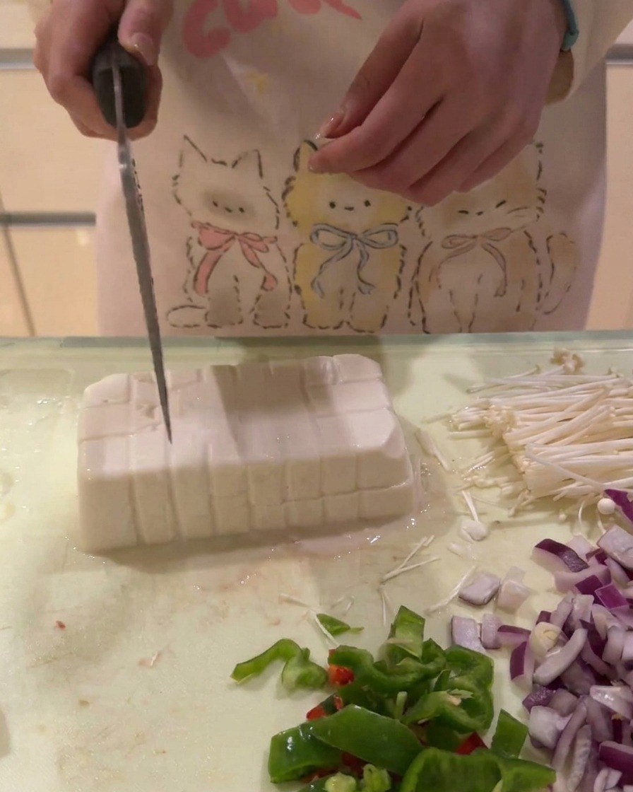 A block of white tofu being sliced into a grid of small cubes on a cutting board.