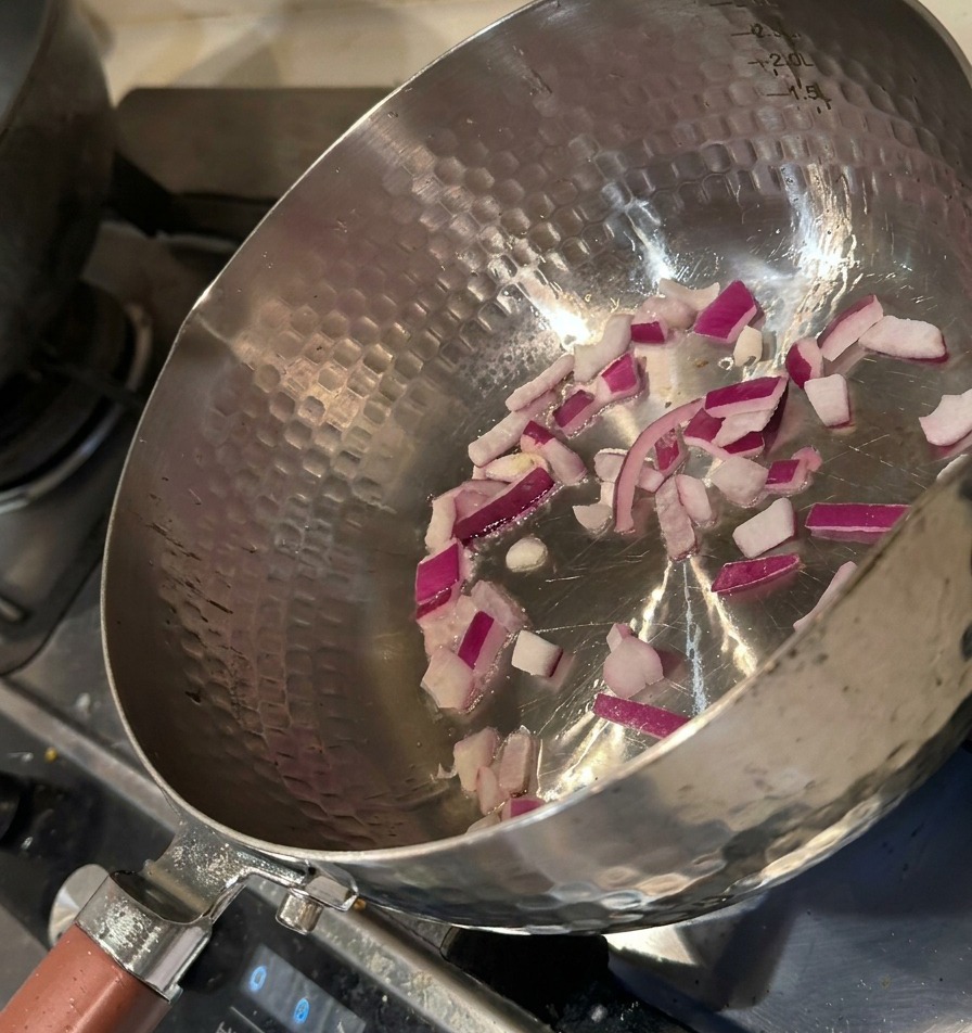Chopped red onions being sautéed in a hot metal pot with a light coating of oil.