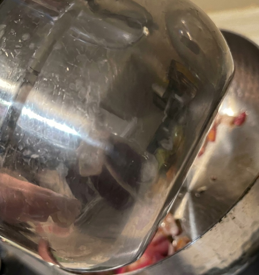 Water being poured from a stainless steel cup into a pot with sautéed red onions.
