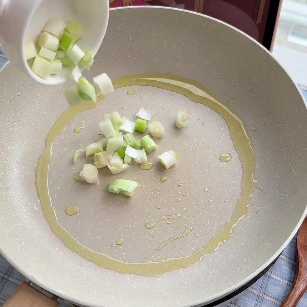 Chopped scallions and leeks being gently stir-fried in a cooking pan with oil.