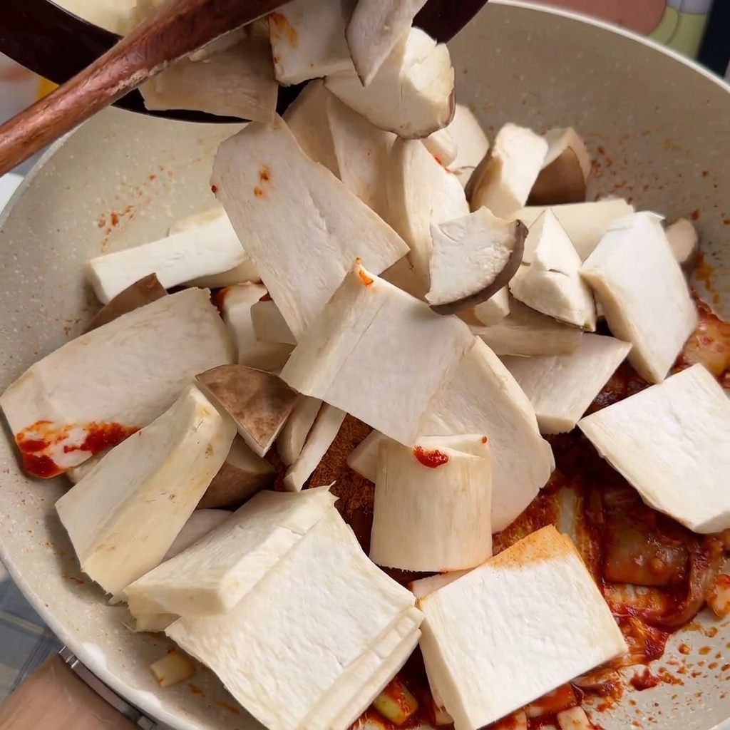 Sliced king oyster mushrooms being dropped into a pan and tossed with a red chili base.