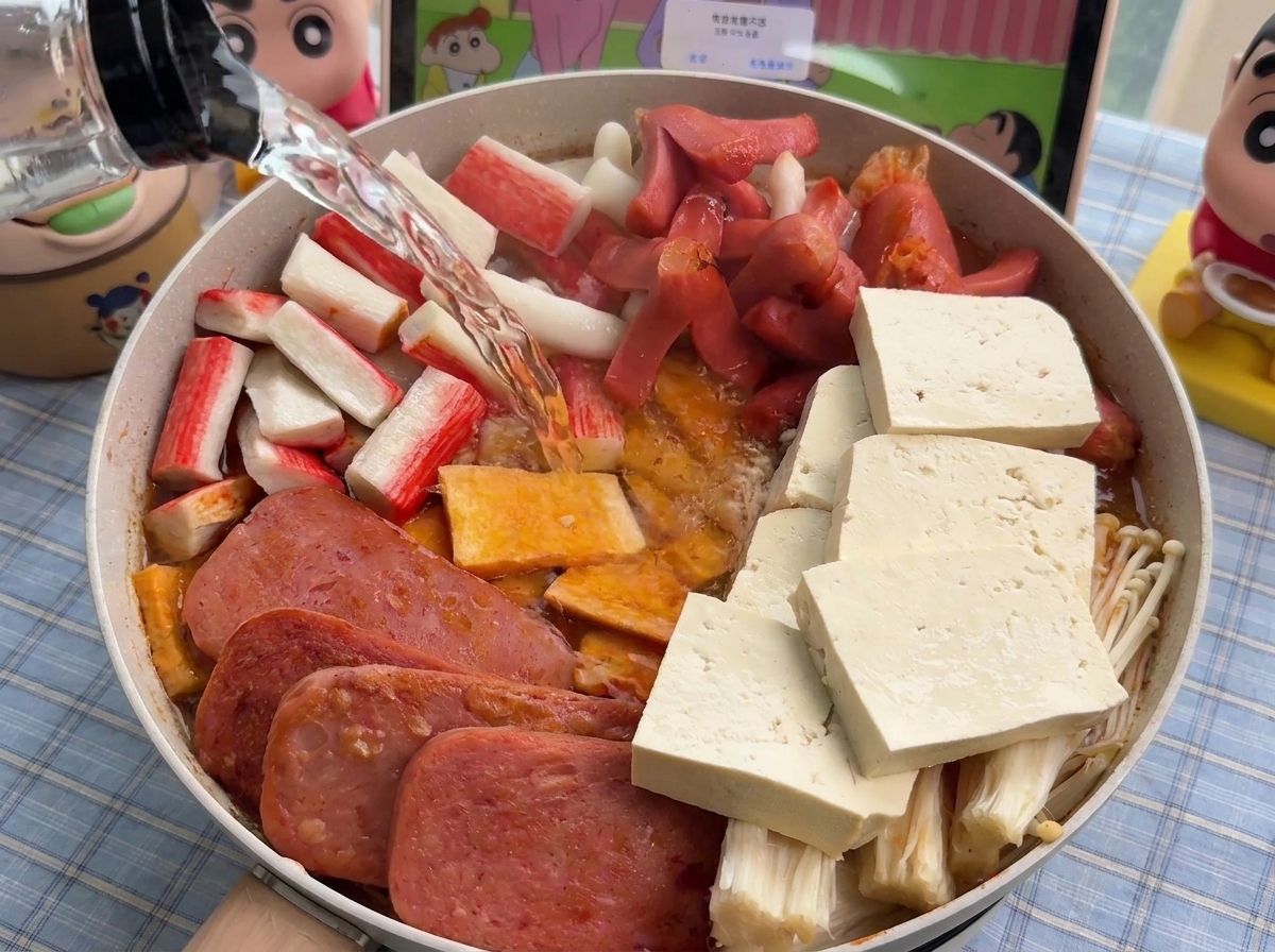 Clear hot water being poured from a bottle into a pan filled with neatly arranged stew ingredients.