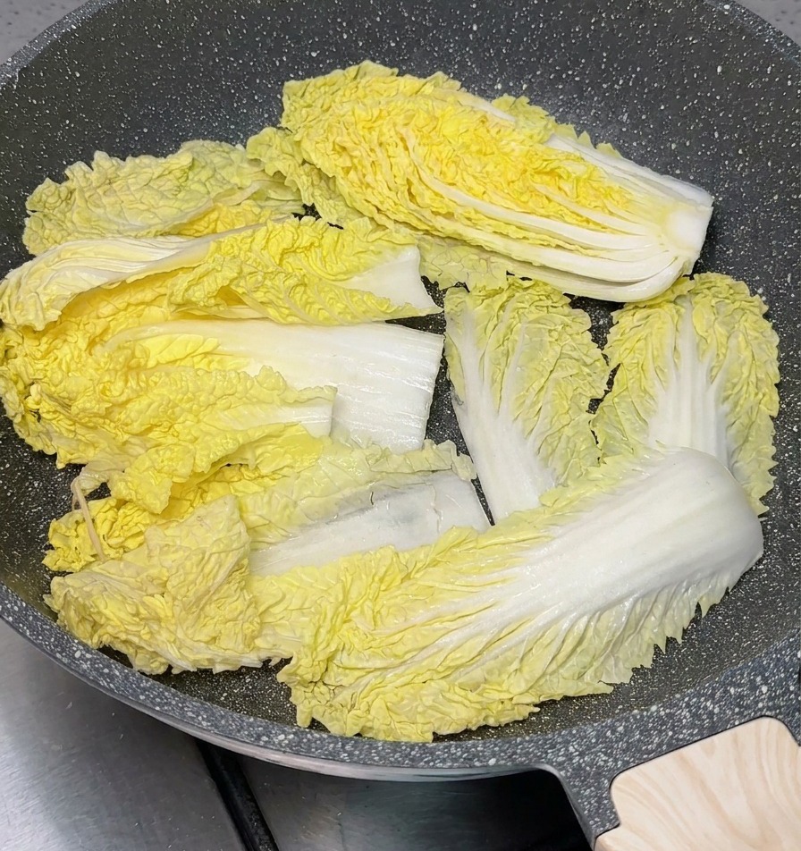Fresh yellow-green Napa cabbage sections arranged to cover the bottom of a grey speckled non-stick cooking pot.
