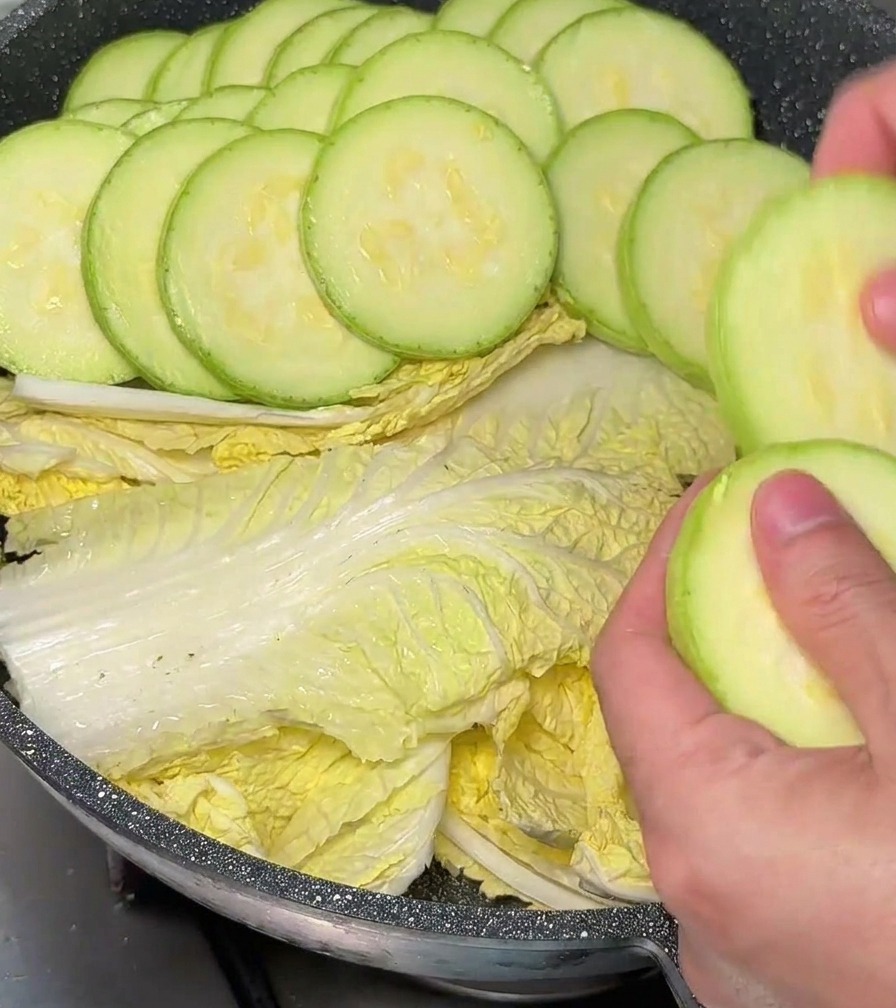 Hands carefully placing green zucchini rounds in an overlapping circular pattern inside a pot lined with cabbage.