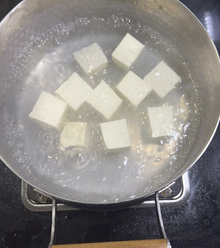 Cubes of white silken tofu simmering in a boiling pot of diluted clam broth on a stovetop.