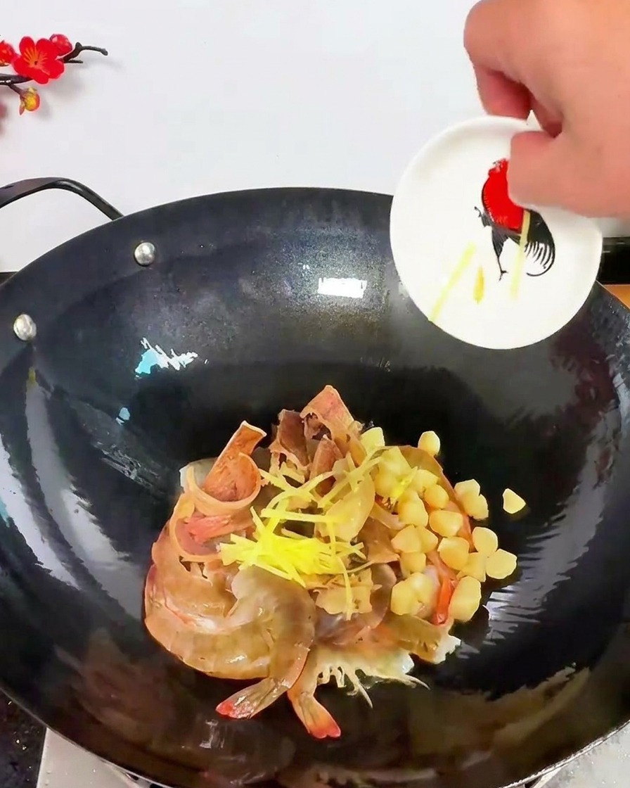 Bright yellow ginger slivers being scattered over a mixture of raw shrimp and dried scallops in a dark wok.