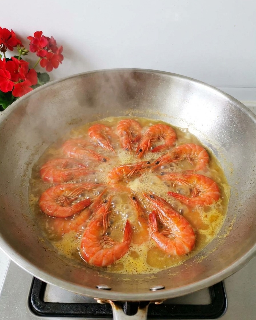 Fresh orange shrimp boiling in a light yellow broth inside a stainless steel wok with steam rising.