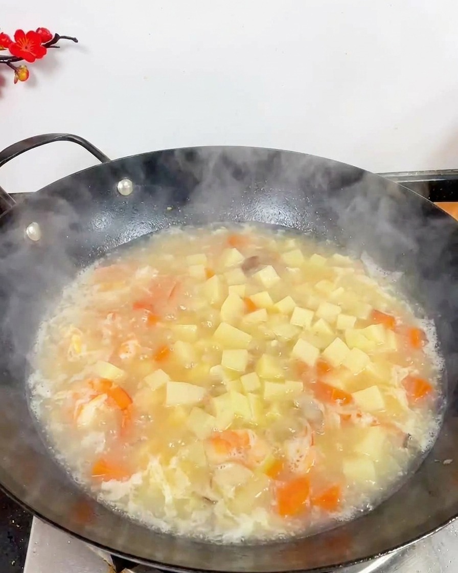 A top-down view of a wok filled with boiling white soup, featuring many cubes of white tofu, shrimp, and small brown mushrooms.
