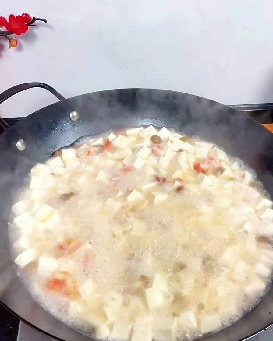A stainless steel ladle pouring dark vinegar into a bubbling white soup filled with tofu and seafood.
