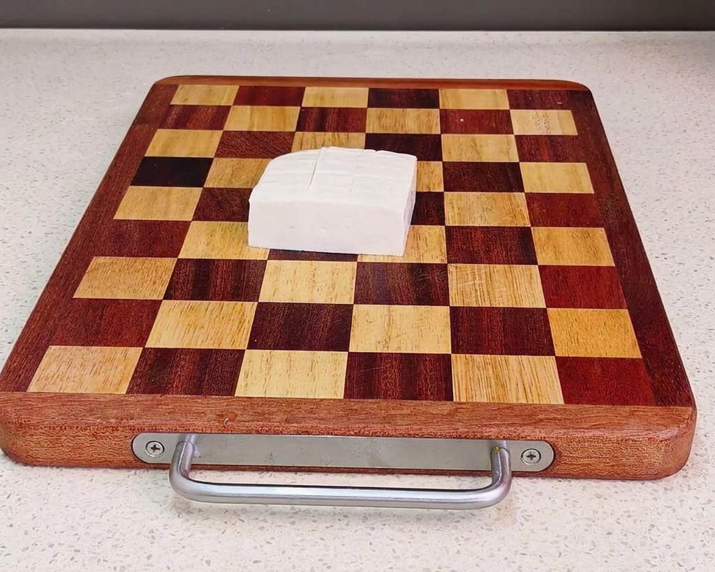 A block of fresh white tofu sliced into uniform cubes, sitting on a brown and tan checkered wooden cutting board.