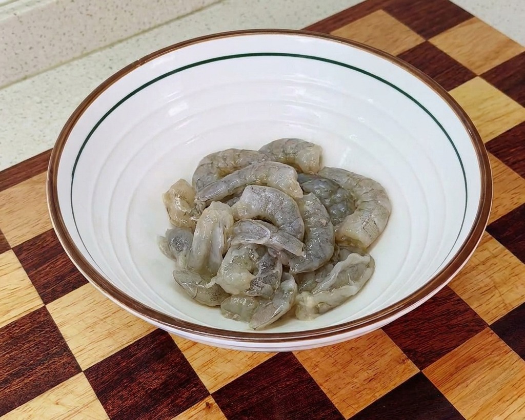A white bowl containing cleaned, raw shrimp meat that has been seasoned with salt, starch, and oil for marinating.