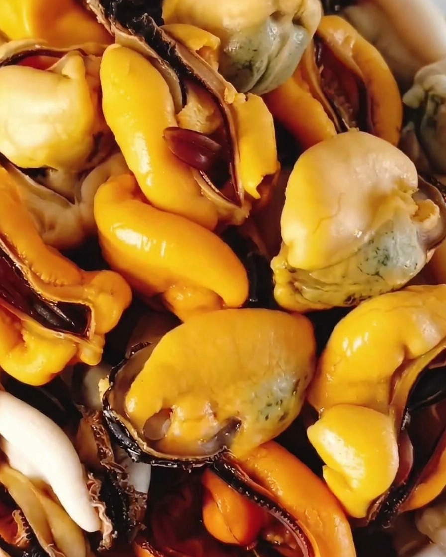 Cooked yellow mussel meat removed from shells and piled in a white bowl