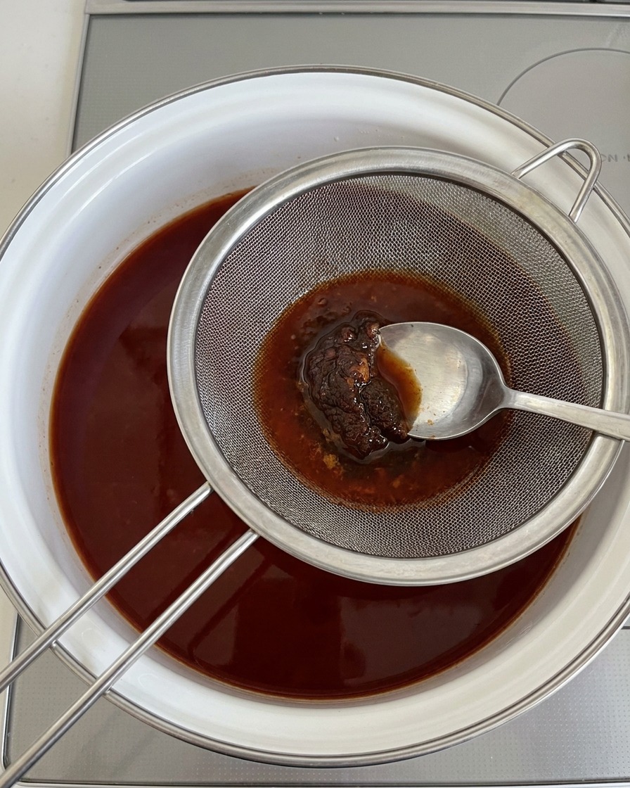 Using a spoon to press thick soybean paste through a metal strainer into boiling broth.