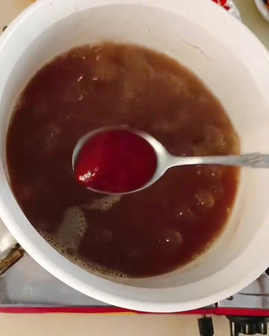 A spoonful of red chili paste being stirred into a pot of bubbling dark brown soup base.