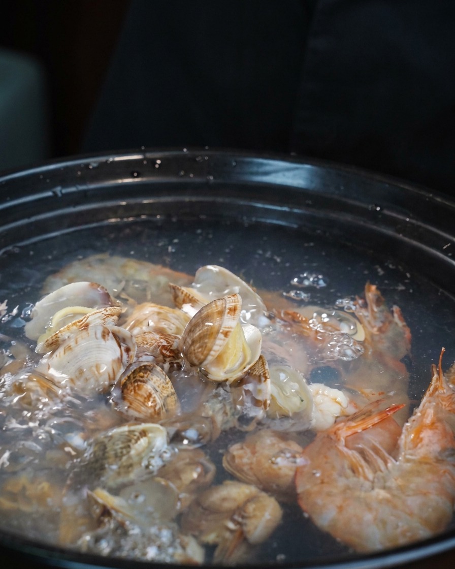 Pale pieces of raw octopus tentacles being added to the pot of boiling seafood soup.