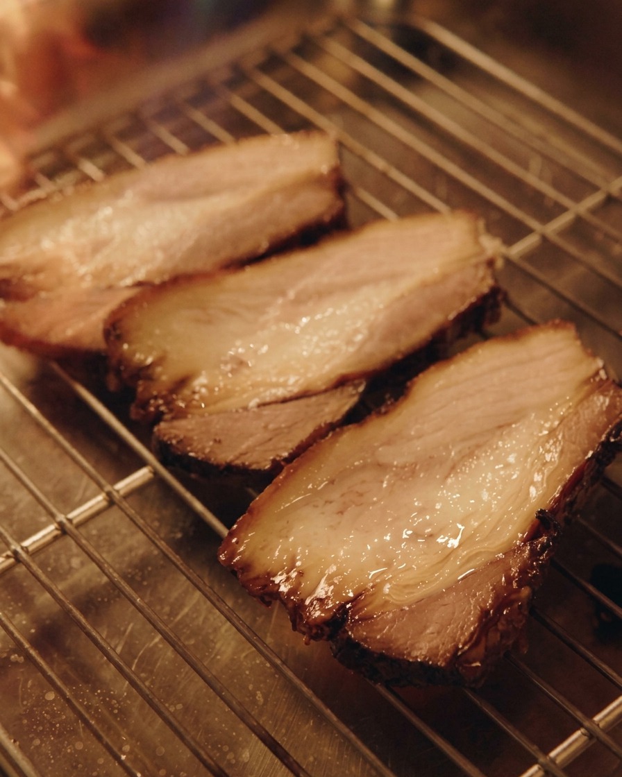 A kitchen blowtorch searing three thick slices of pork chashu resting on a metal wire rack.