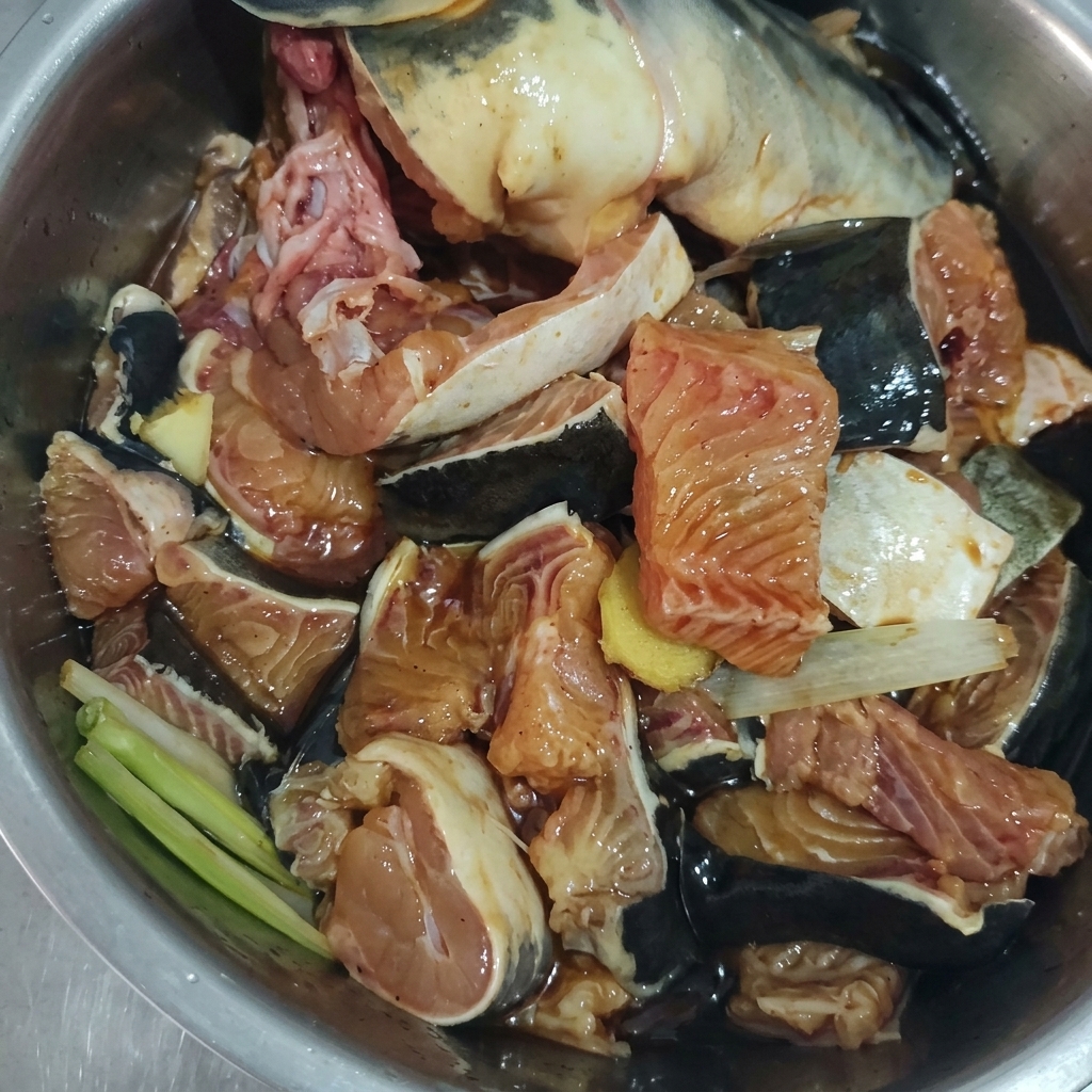 Raw fish chunks mixed with ginger, scallions, and dark marinade in a metal bowl.
